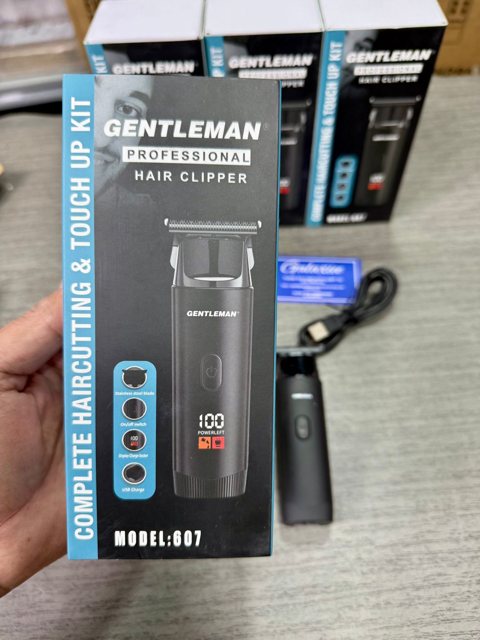 Gentleman professional hair clipper packaging held by a hand with additional products in the background.