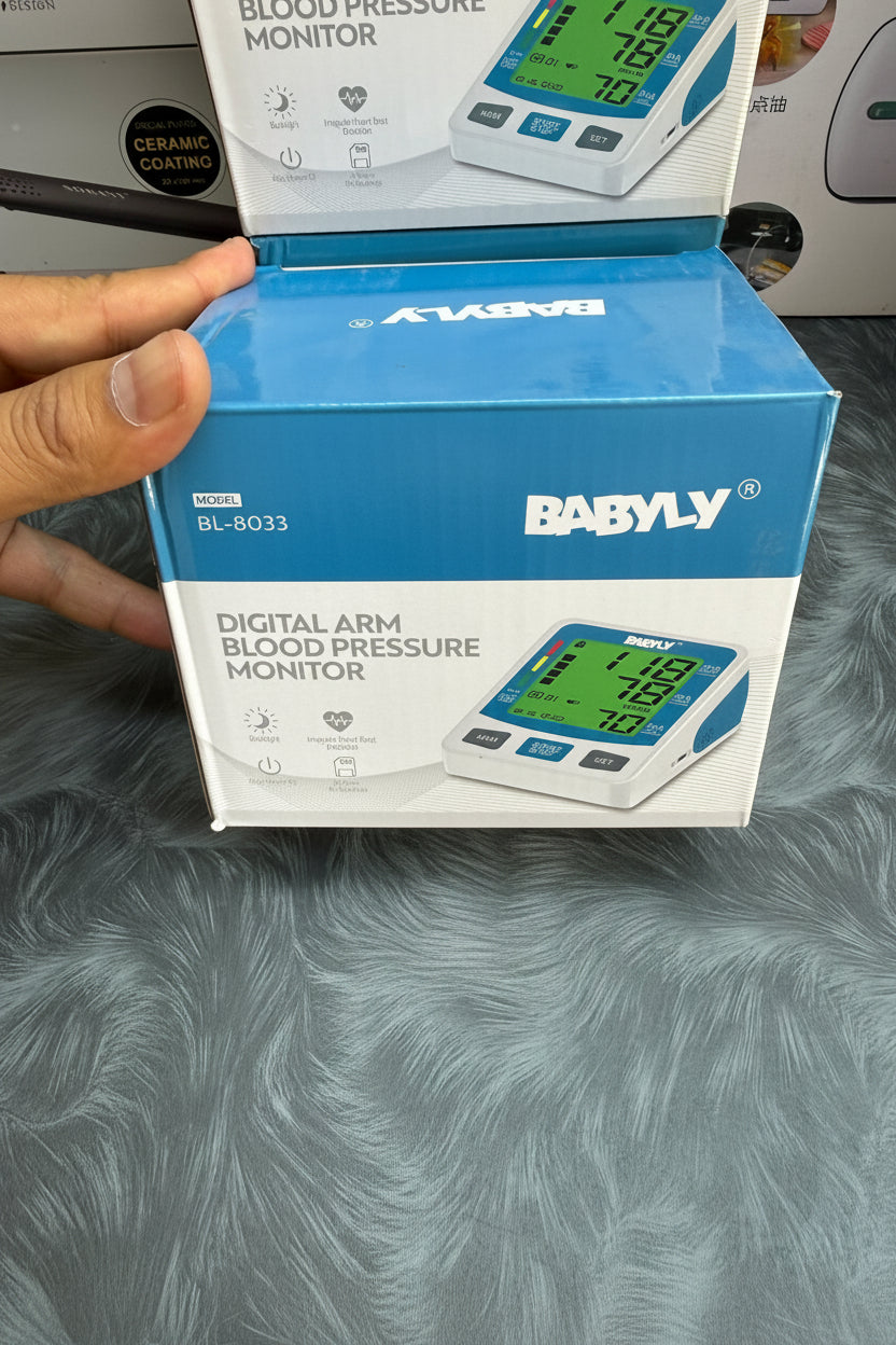 Babyly digital arm blood pressure monitor packaging held by a hand on a textured surface.